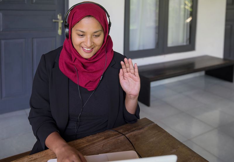Woman waving hello while on a video job interview.