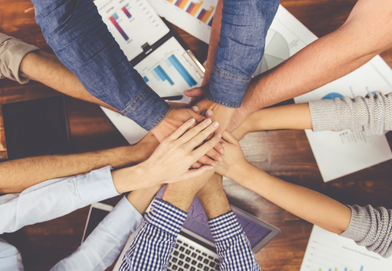 A group of individual's hands overlapping each other over a work table.
