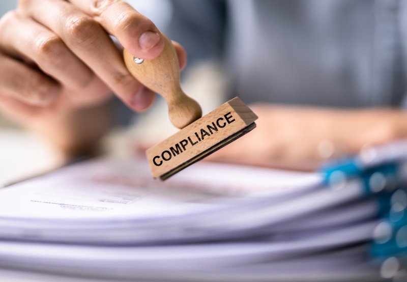 Hand stamping a stack of tax, labour, employment law and worker classification guidelines with a stamp that says compliance.