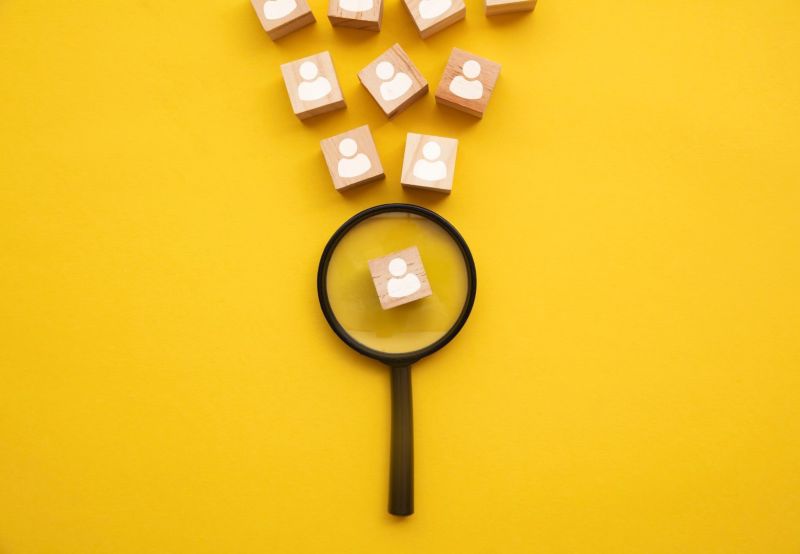 Yellow background with a magnifying glass highlighting a persona.  