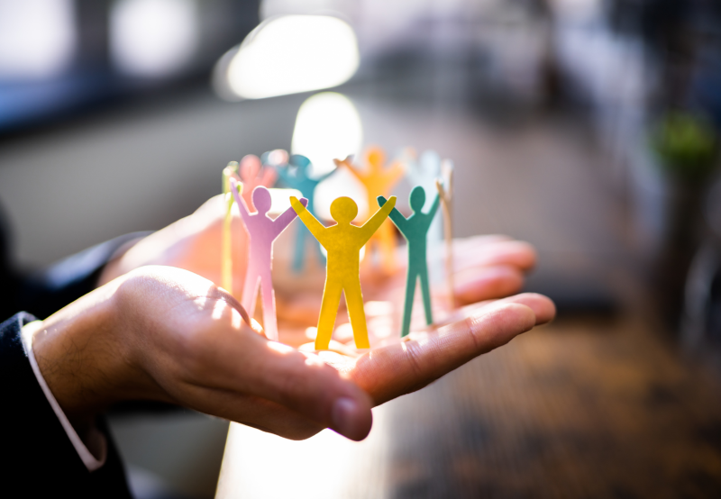 Persons hands holding paper cutouts of people standing in a circle holding hands.