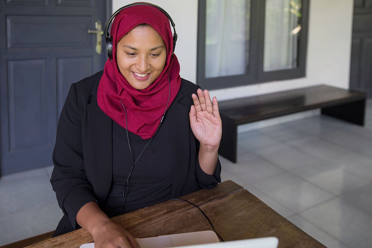 Woman waving hello while on a video job interview.