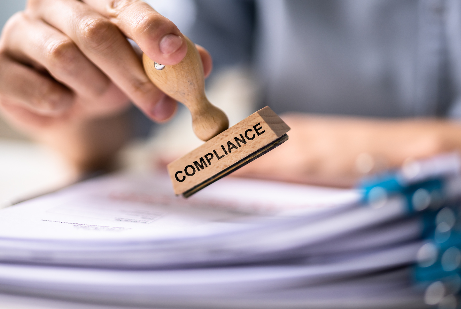 Hand stamping a stack of tax, labour, employment law and worker classification guidelines with a stamp that says compliance.
